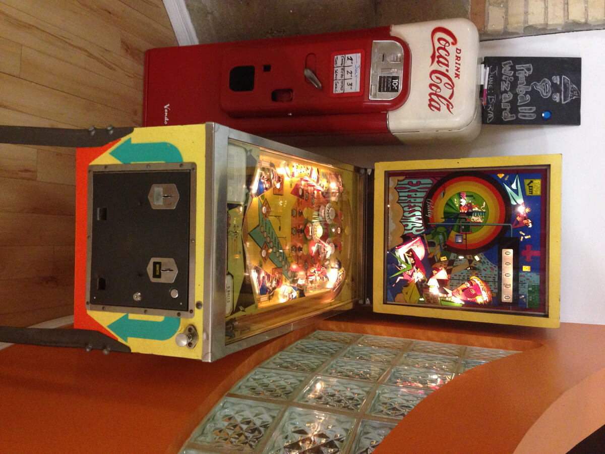 Picture of a yellow, green and orange Expressway Pinball machine beside a red and white Coca-Cola machine